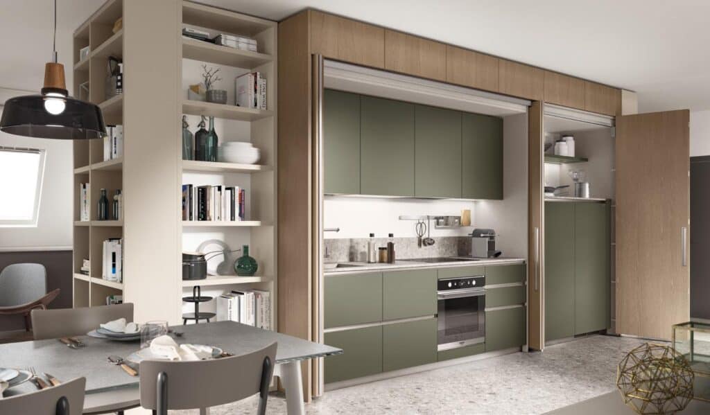 Modern kitchen and dining area with olive green cabinetry, built-in shelving, and a dining table set with plates and cutlery.