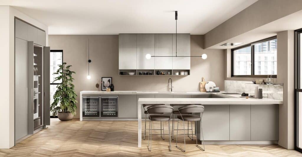 Modern kitchen with light gray cabinets, marble countertops, a large island with bar stools, pendant lighting, and a potted plant by the window.