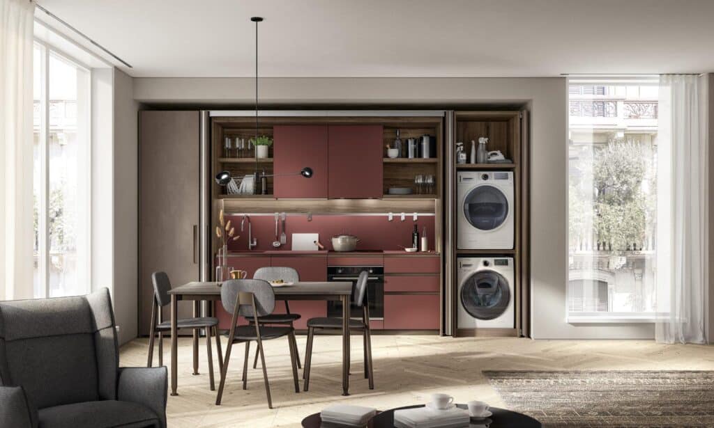 Modern kitchen with red cabinets, integrated dining table, and stackable washer and dryer.