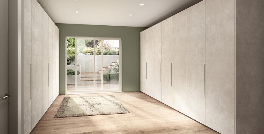 A spacious room with white built-in wardrobes on both sides, a large window at the end, and a rug on a wooden floor.