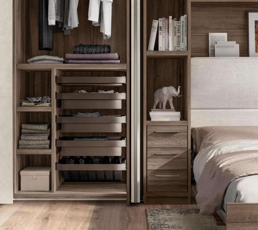 Bedroom with an open wardrobe, shelves with clothes, a nightstand with books and an elephant figurine, and part of a bed.