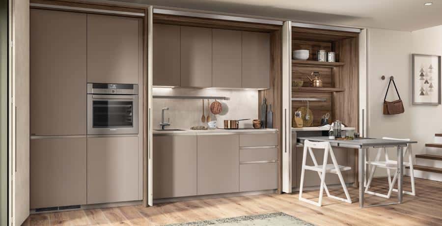 Modern kitchen with beige cabinets, built-in oven, and minimalistic decor, featuring a small dining table with two chairs.