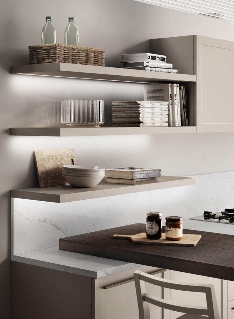 Modern kitchen with illuminated floating shelves, holding glassware, books, and decorative items; a countertop with jars and a wooden cutting board is visible.