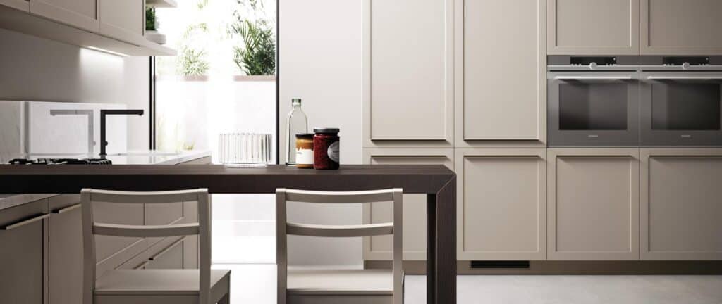Modern kitchen with beige cabinetry, dark wooden table, white chairs, a gas cooktop, built-in ovens, and a large window.