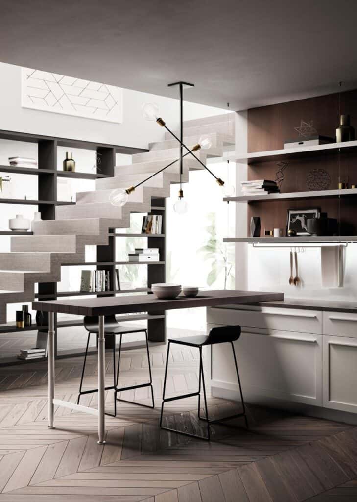 Modern kitchen interior with a minimalist design, featuring a geometric staircase, sleek barstools at an island, and open shelving with decor items.
