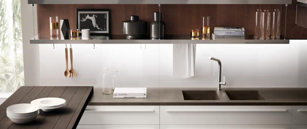 Modern kitchen with wood and metal shelving, decorative items, a sleek faucet, dual sinks, and stacked white dishes.
