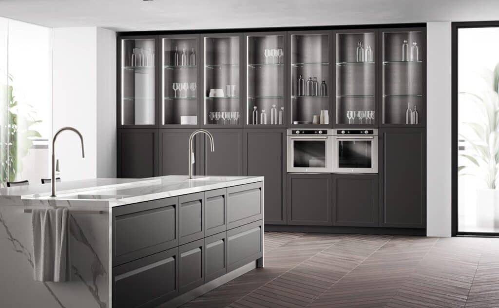Modern kitchen with dark cabinetry, glass display cabinets, a marble island with dual sinks, and built-in ovens.