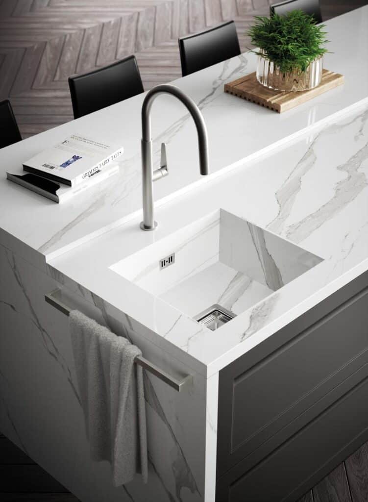 Modern kitchen island with a marble countertop, integrated sink, stainless steel faucet, a potted plant, and a towel hanging on the side.