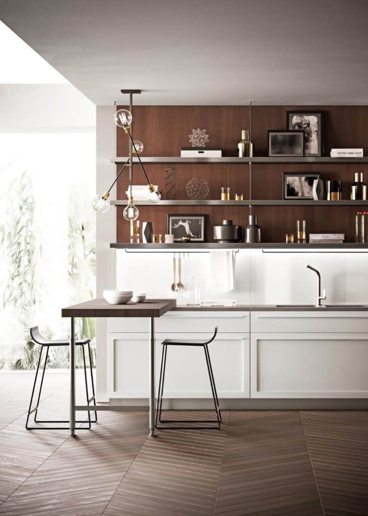 Modern kitchen with a white island and dark wood top, two black bar stools, open shelving with decorative items, and a contemporary light fixture.