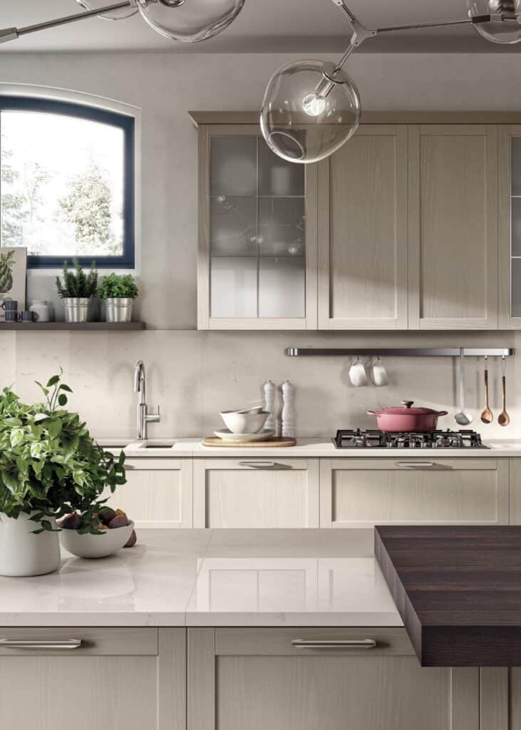 Modern kitchen with light-colored cabinets, a large window, shelves with plants, a gas stove with a pink pot, and a marble countertop with greenery.