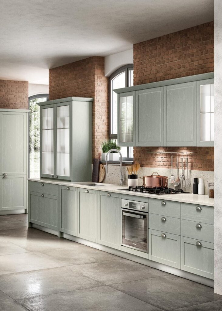 Modern kitchen with light green cabinets, brick walls, and stainless steel appliances.