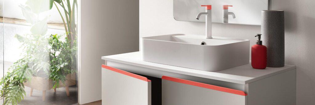 Bathroom vanity with a rectangular sink and mirror, red accents on faucet and cabinet handles, red soap dispenser, and potted plants nearby.