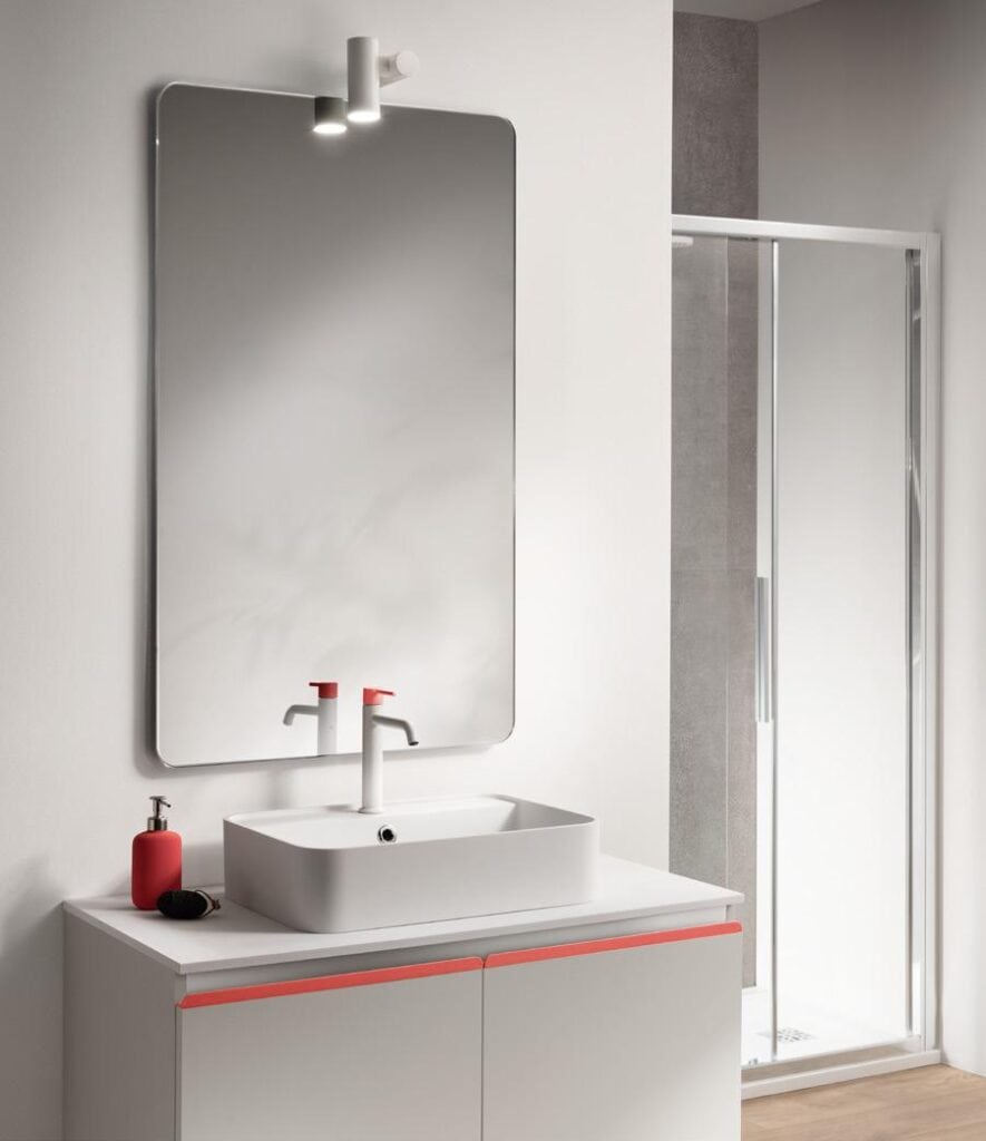 Modern bathroom with a large mirror, minimalistic white sink, red-accented faucet, and a soap dispenser on a vanity.