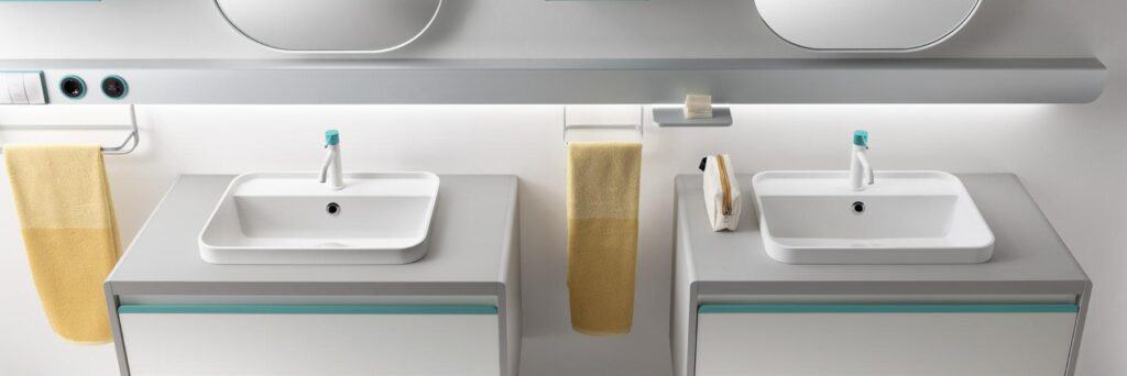 Modern bathroom with two white rectangular sinks, light gray countertops, mirrors, and yellow towels.