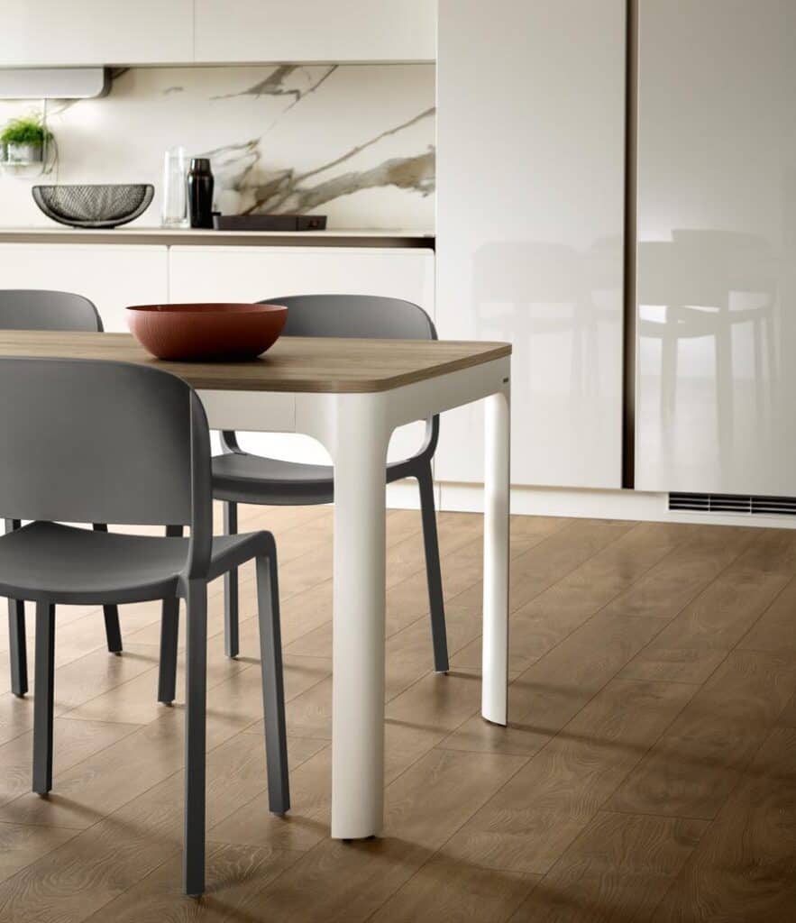 Modern kitchen with a wooden table, gray chairs, and a brown bowl, featuring a marble backsplash and white cabinets.