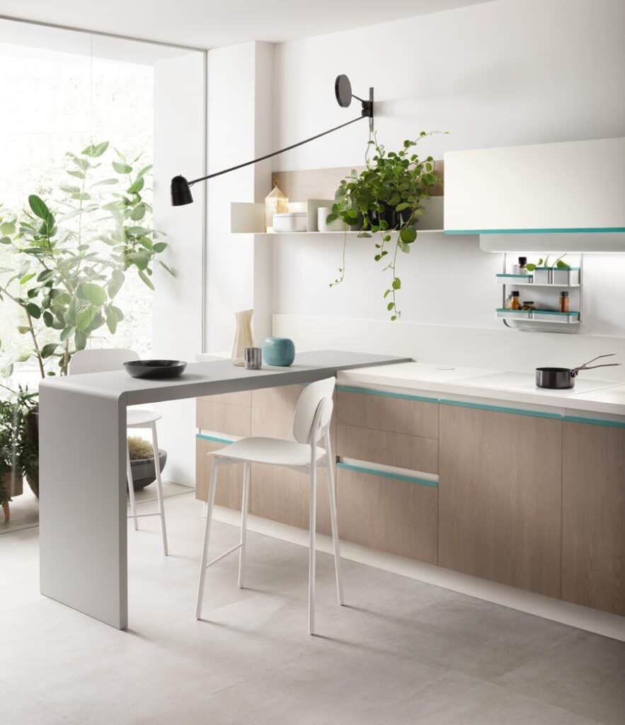 Modern kitchen with a minimalist design featuring light wood cabinetry, a small breakfast bar with a white chair, wall-mounted shelves with potted plants, and a sleek, adjustable wall lamp.