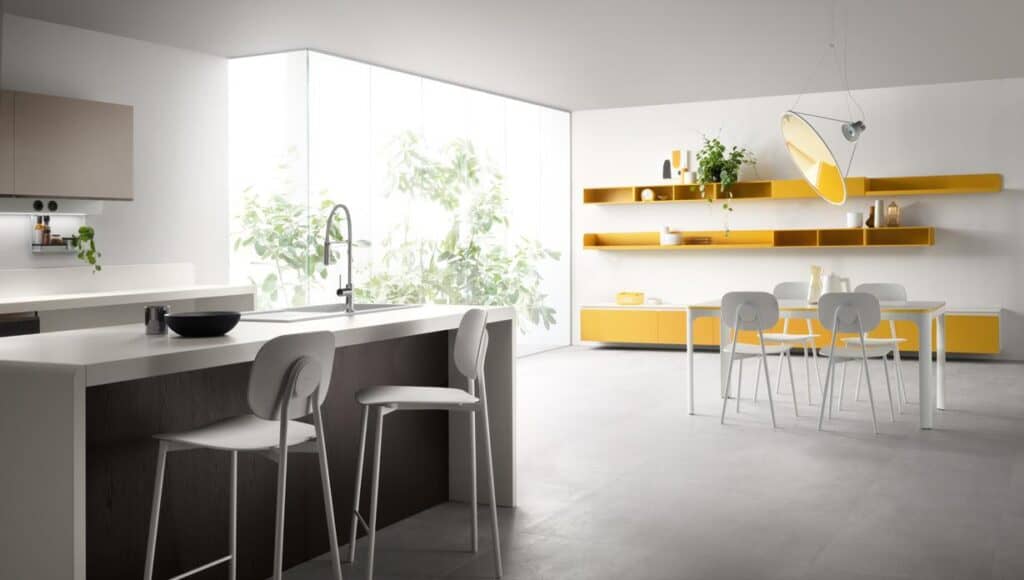 Modern kitchen and dining area with white and yellow decor, featuring a large window, sleek countertops, and minimalist furniture.