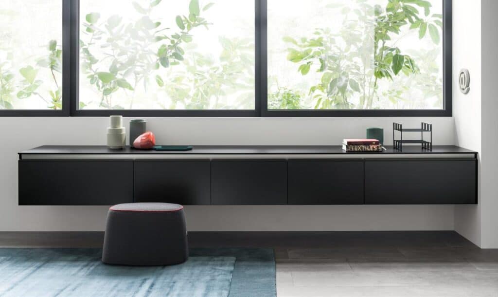 Modern interior with a black floating sideboard beneath large windows, decorated with small objects, and a stool in front.