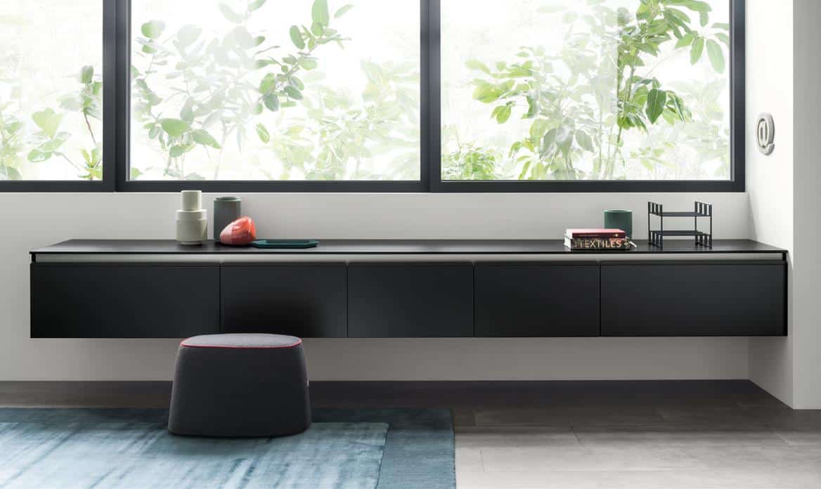 Modern interior with a black floating sideboard beneath large windows, decorated with small objects, and a stool in front.