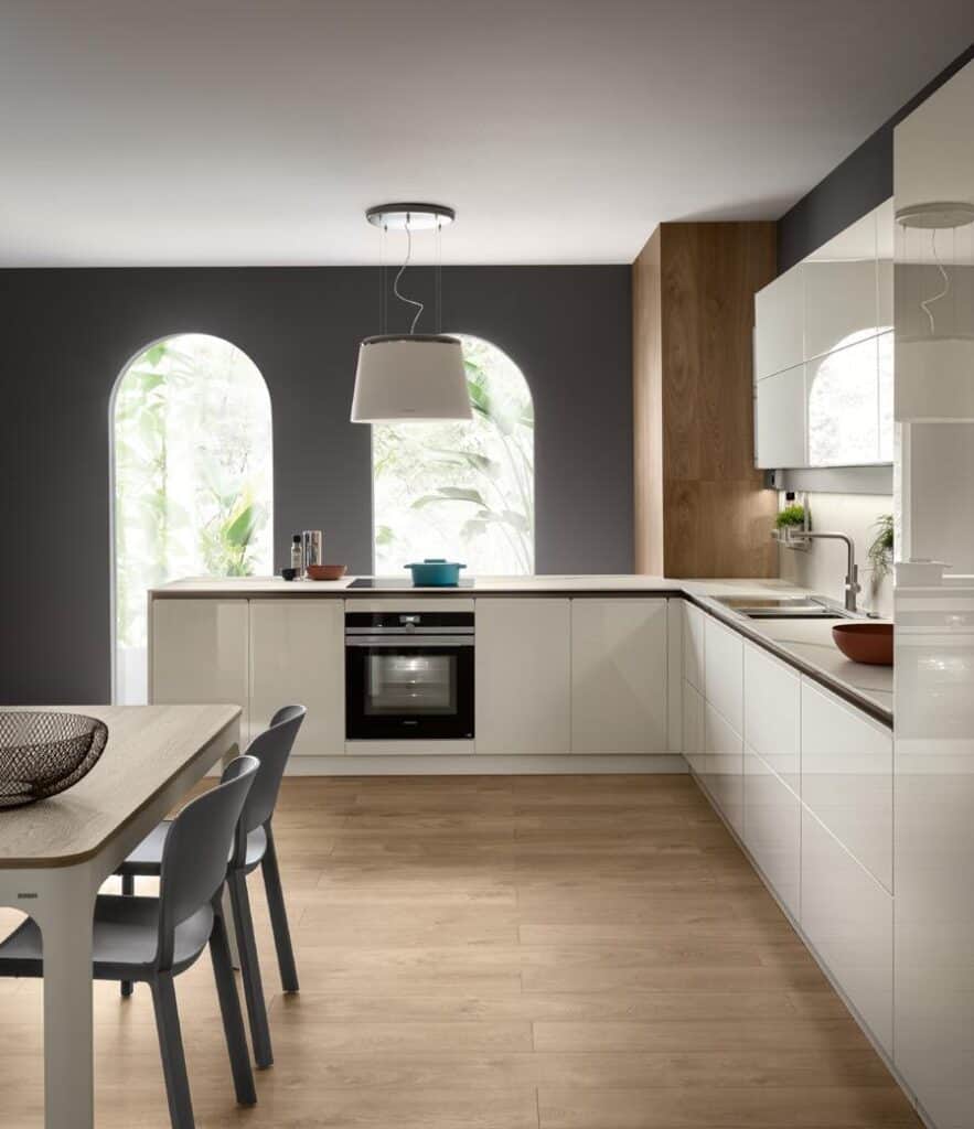 Modern kitchen with white cabinets, wood flooring, a dining table with chairs, and a large ceiling light fixture.