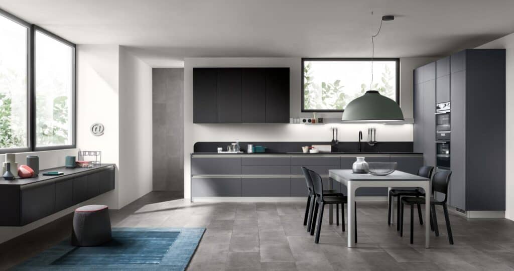 Modern kitchen with dark cabinetry, light gray countertops, a dining table with black chairs, large windows, and a green pendant light.