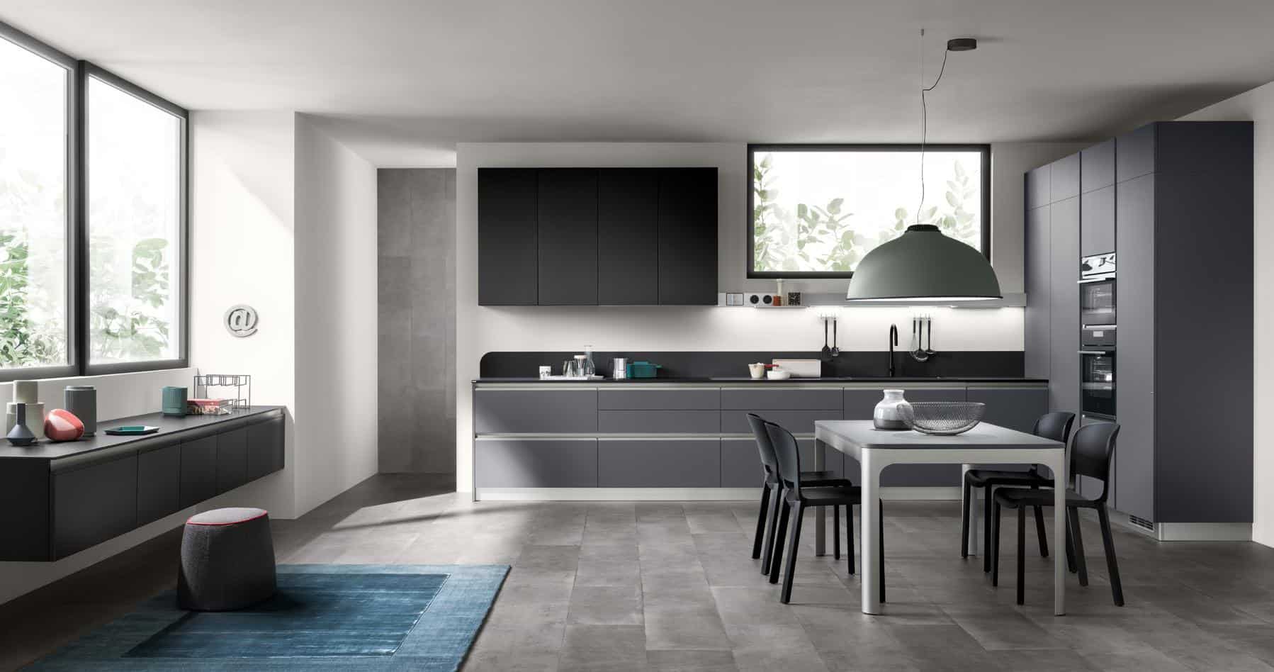 Modern kitchen with dark cabinetry, light gray countertops, a dining table with black chairs, large windows, and a green pendant light.