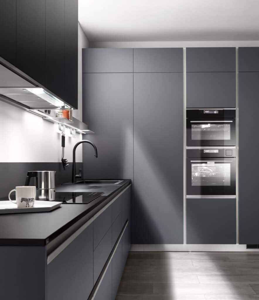 Modern kitchen with dark cabinetry, built-in ovens, induction cooktop, and a sleek black faucet.