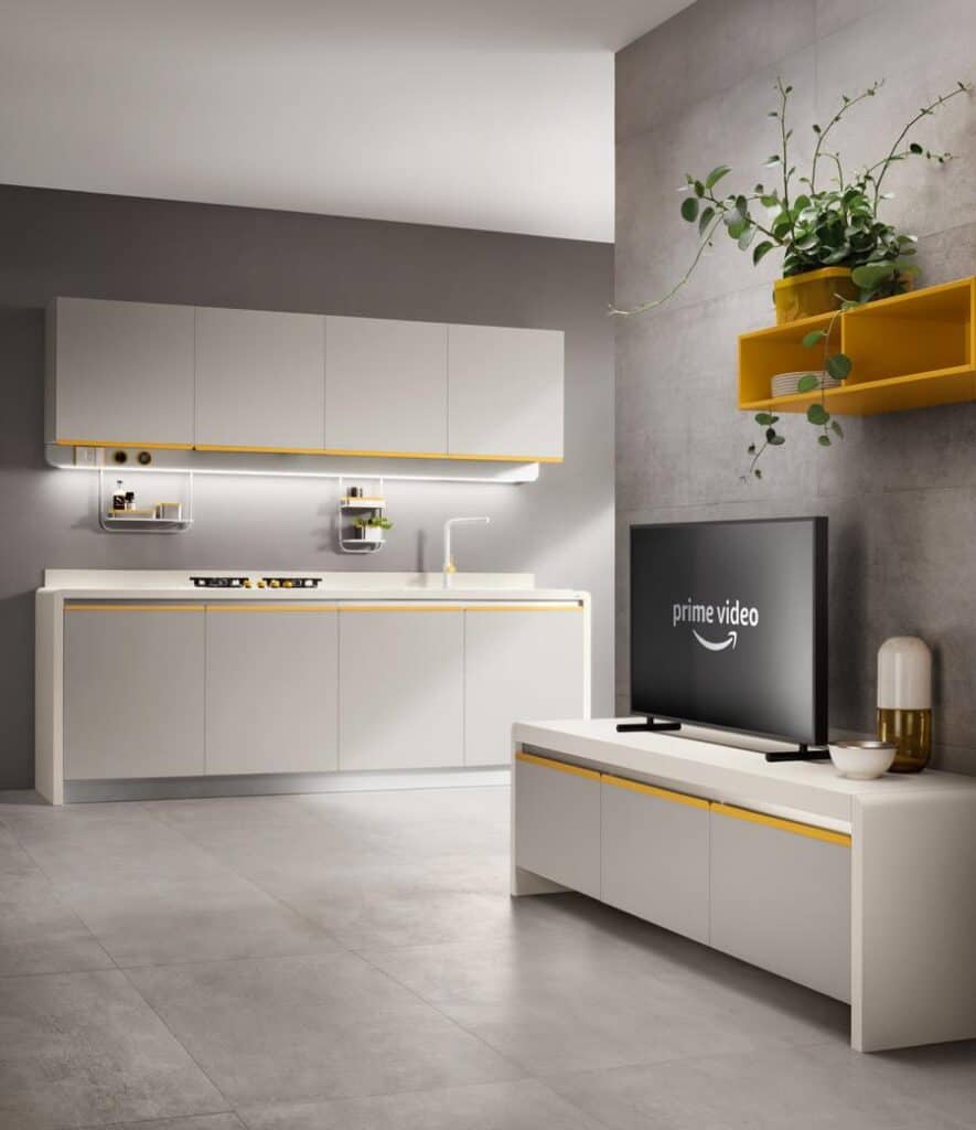 Modern kitchen interior with sleek cabinets, a mounted TV displaying &quot;Prime Video,&quot; and a yellow accent shelf with a plant.
