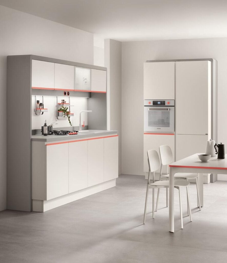 Modern kitchen with white cabinetry, built-in oven, stovetop, dining table, and chairs, featuring red accents.