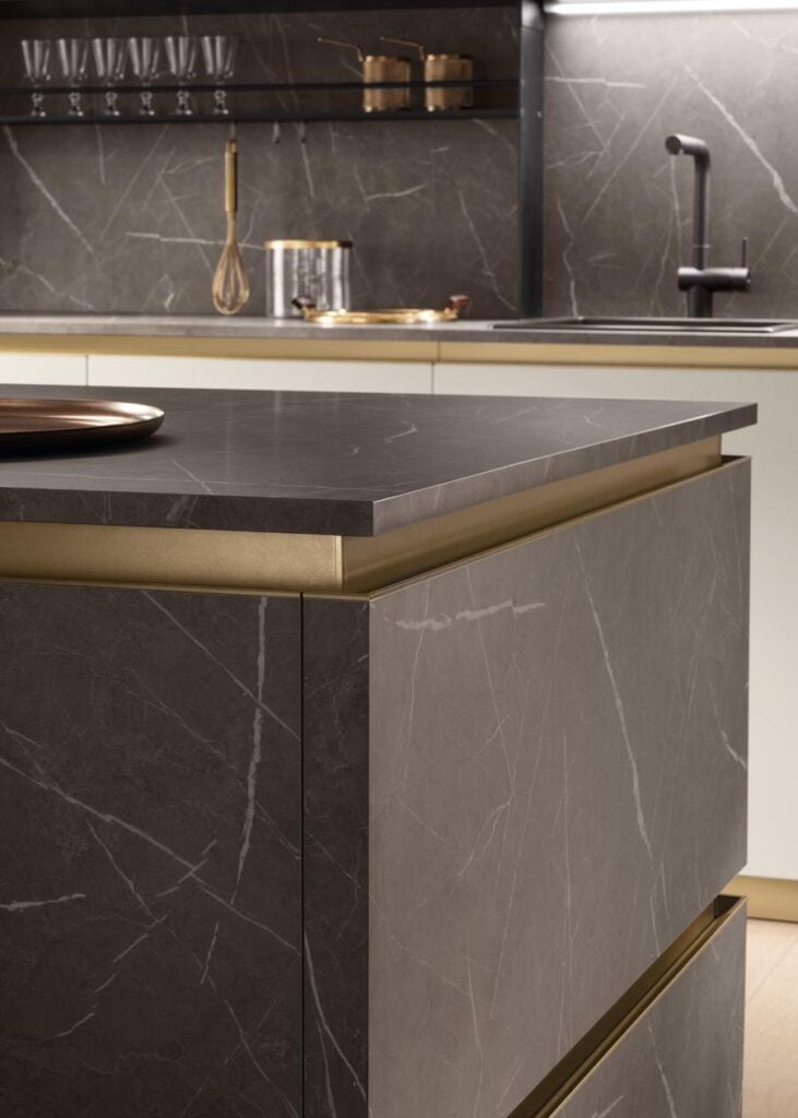 Modern kitchen with dark marble countertops and gold accents, featuring a sink and utensils on the counter.
