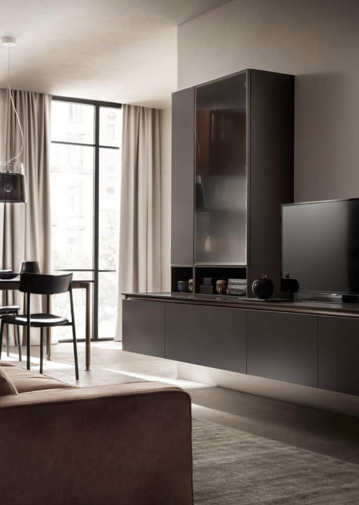 Modern living room with dark furniture, large window with curtains, dining table with chairs, and a TV on a cabinet.
