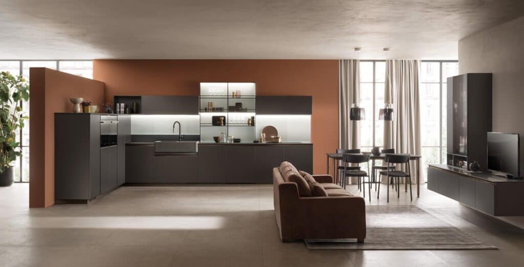 Modern open-concept kitchen and living area with dark cabinets, a brown sofa, dining table with chairs, and large windows with curtains.