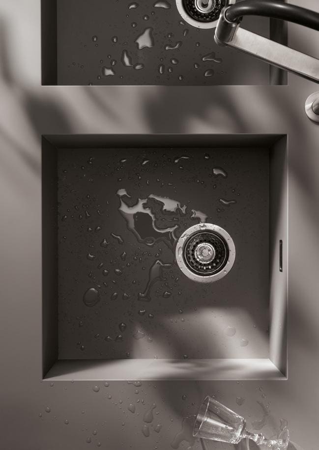 Stainless steel sink with water droplets, a faucet, and a glass lying on the counter.