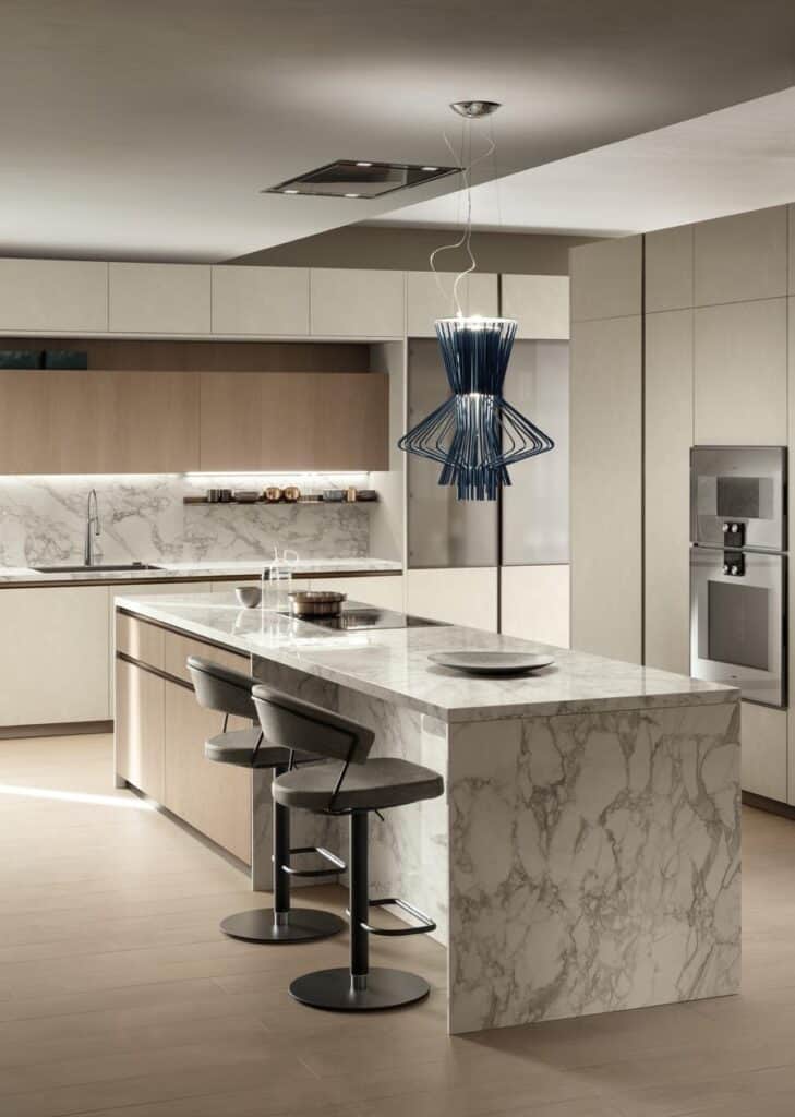 Modern kitchen with marble countertops, light wood cabinetry, sleek barstools, and a unique blue pendant light above the island.