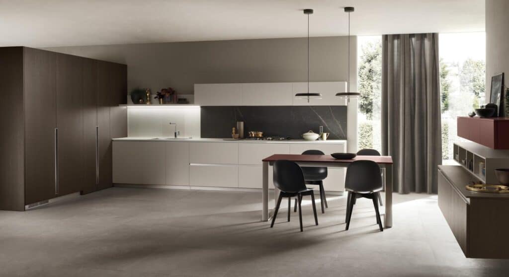 Modern kitchen interior with dark wood cabinets, white countertops, a red dining table, and black chairs, illuminated by pendant lights.
