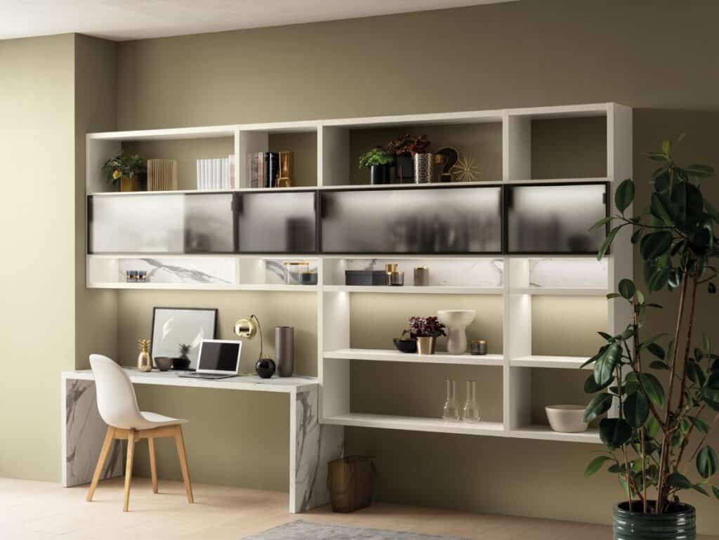 Modern home office with a white chair, marble desk, laptop, decorative items, and wall-mounted shelves in a room with green walls.