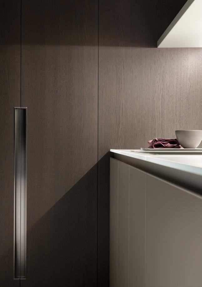 Sleek modern kitchen with dark wood cabinets, a gray handle, and a white counter with a bowl and folded cloth.