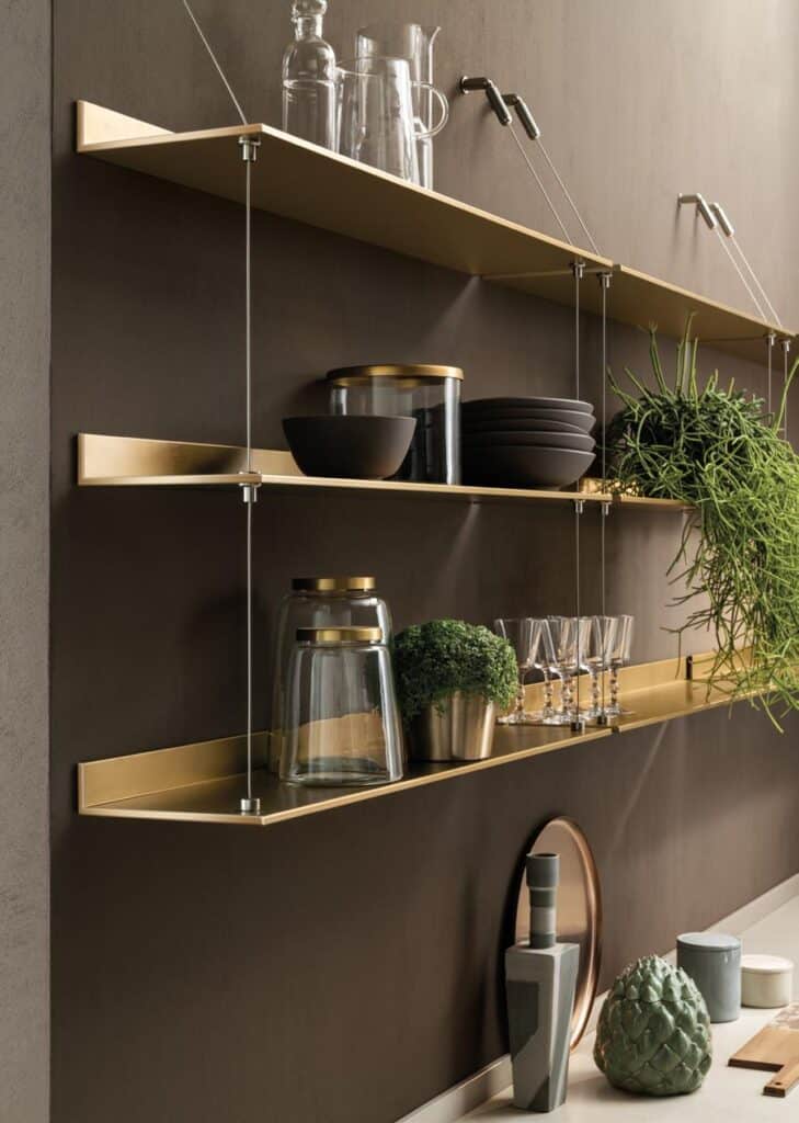 Wall-mounted gold shelves with glassware, black bowls, storage jars, a potted plant, and a green ornament.