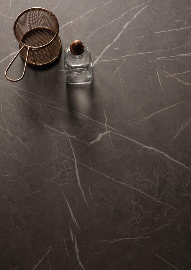 A brass sieve and a small glass bottle with a cork stopper on a dark marble surface with white veining.