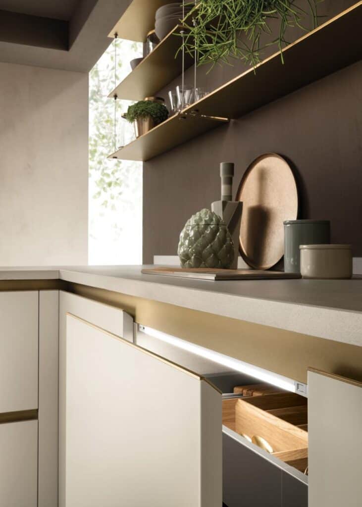 Modern kitchen corner with open drawer underneath a minimalist countertop, decorative plants, and utensils on display shelves.