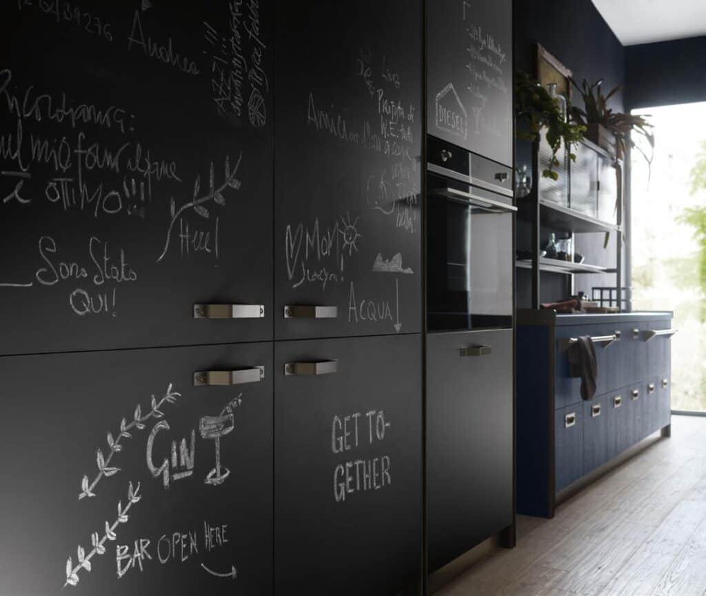 Chalkboard kitchen cabinets with scribbles and drawings, including words like &quot;GET TOGETHER&quot; and &quot;GIN,&quot; next to an oven.