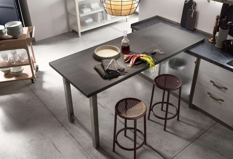 Modern kitchen with a dark wood table, two brown stools, a cart with dishes, and kitchen items like rhubarb and a cutting board.