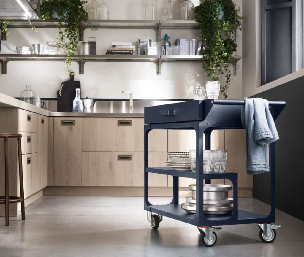 Modern kitchen with light wood cabinets, open shelves, and a blue kitchen cart with wheels holding glassware and dishes.