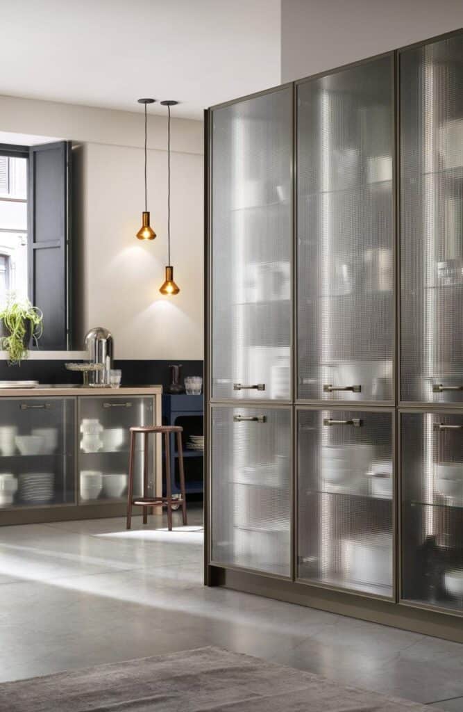 Modern kitchen interior with frosted glass cabinets, a wooden stool, pendant lights, and an arrangement of kitchenware.