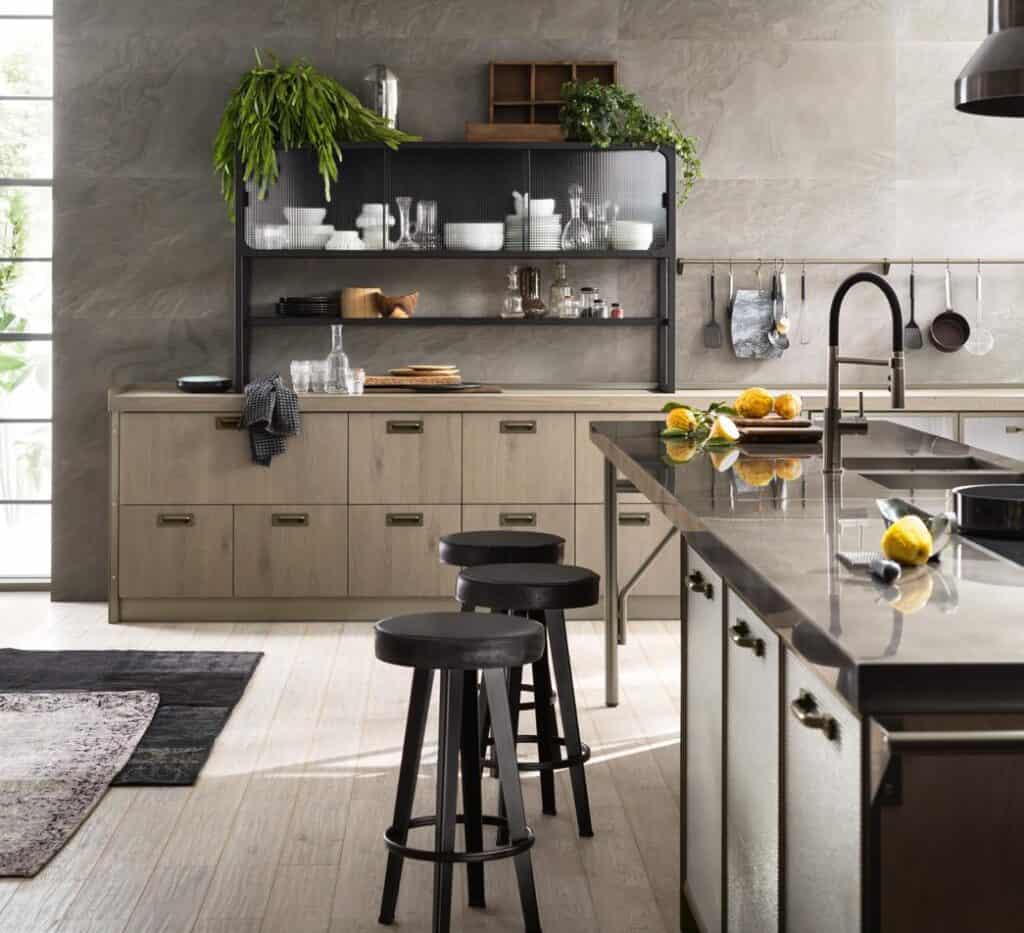 Modern kitchen with wooden cabinets, metal countertops, black stools, open shelves with dishes, and hanging kitchen utensils.