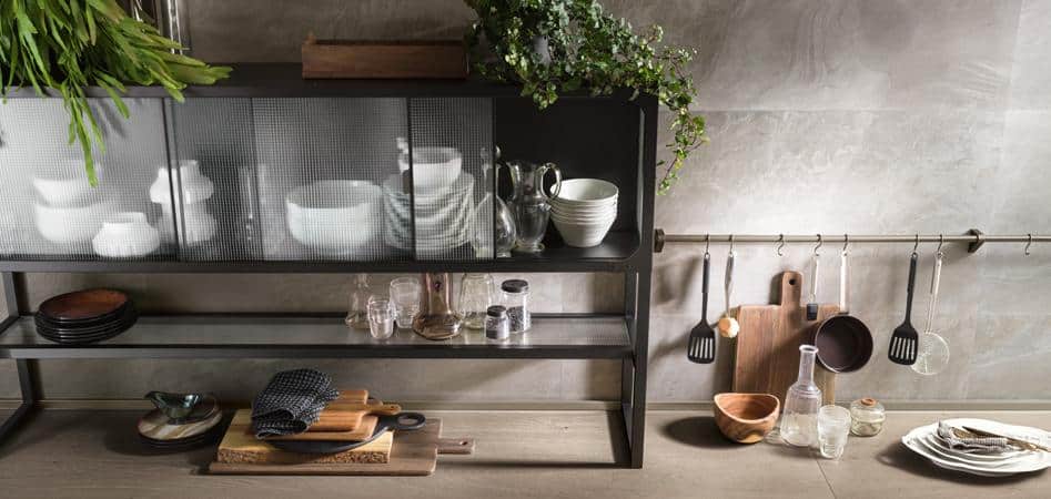 Modern kitchen storage with open shelves displaying dishes, cutting boards, and glassware, alongside a wall rail with hanging kitchen utensils.