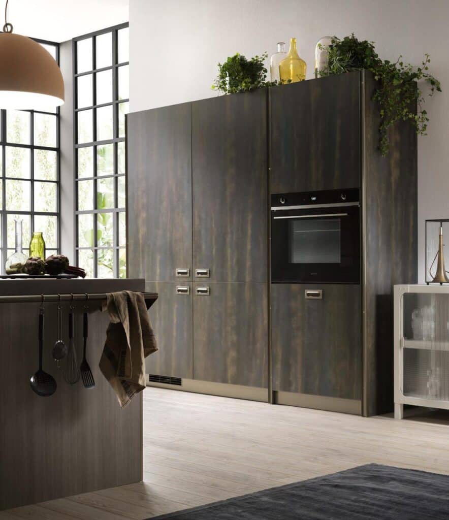 Modern kitchen with dark wood cabinets, built-in oven, large windows, island with hanging utensils, and plants on top of the cabinets.