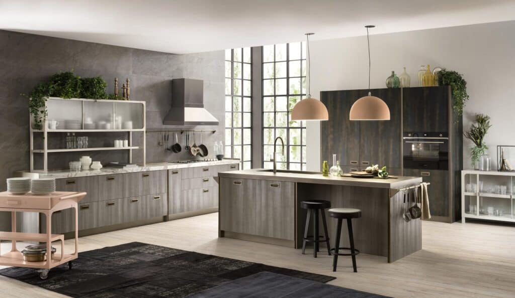 Modern kitchen with gray cabinets, large windows, an island with stools, hanging pendant lights, and various plants and decorative items.