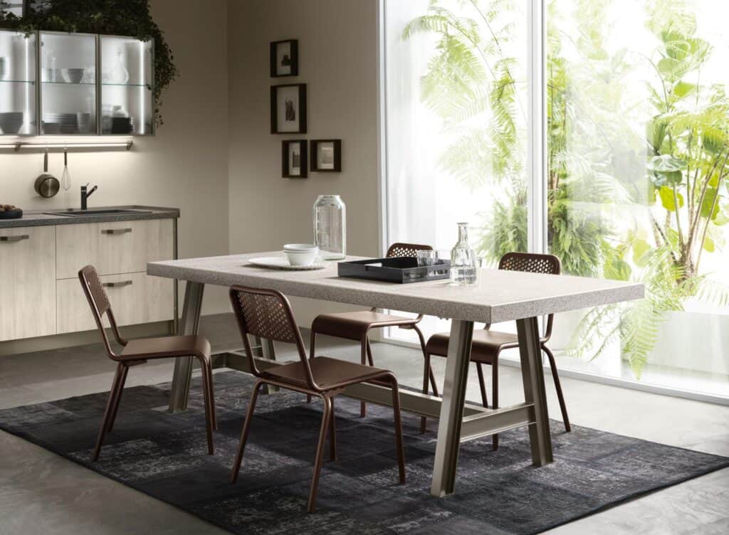 Modern kitchen space with a large dining table, four chairs, potted plants, and glass wall.