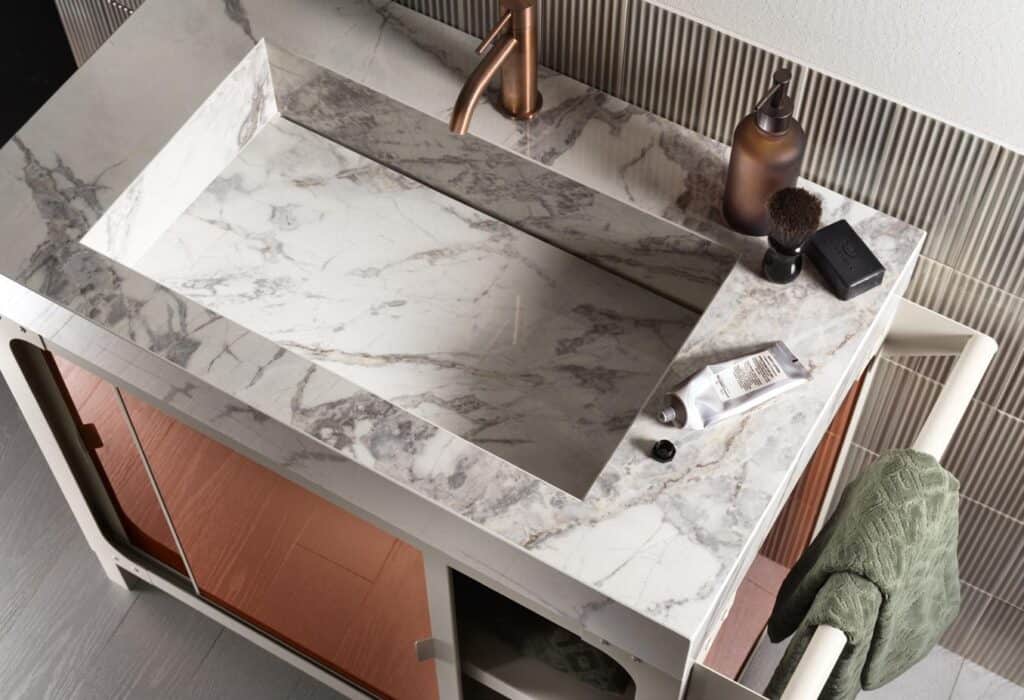 Marble bathroom vanity with integrated sink, copper faucet, and toiletries on the counter including a soap dispenser, shaving brush, and tube.